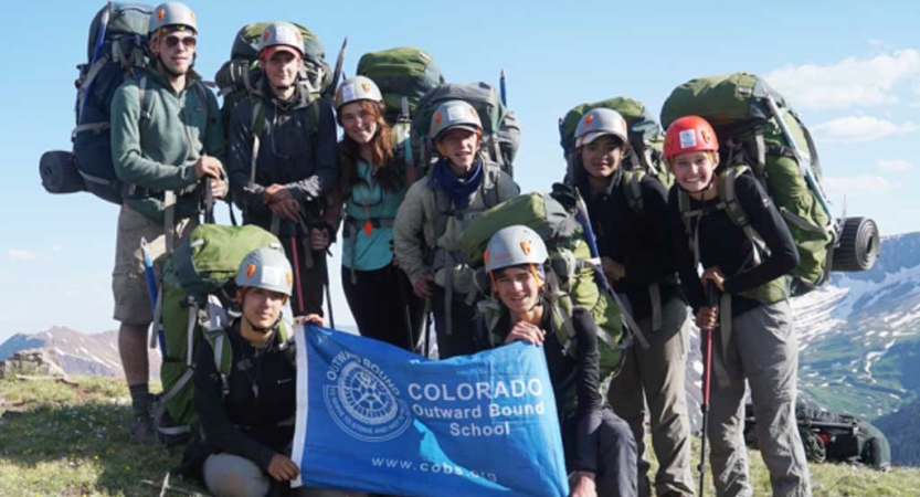 A group of people wearing helmets and backpacks pose for a group photo on a mountain summit 